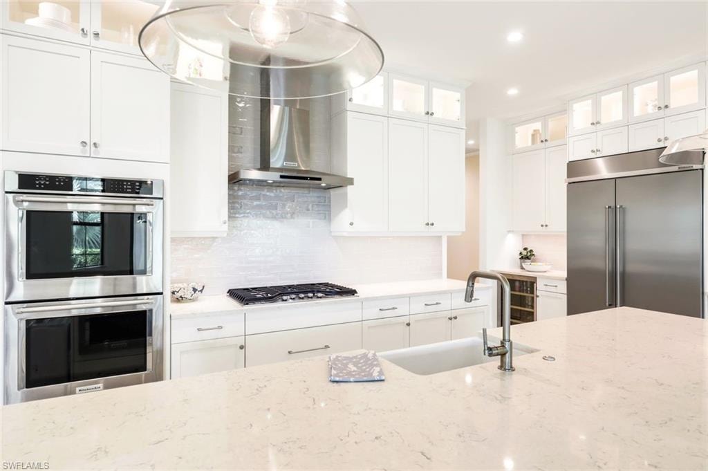 Kitchen with glass fronted cabinets, stainless steel appliances, white cabinets, decorative backsplash, and light stone counters