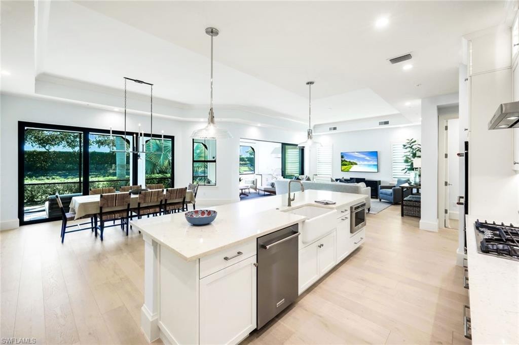 Kitchen with white cabinets, a tray ceiling, open floor plan, an island with sink, and light stone counters