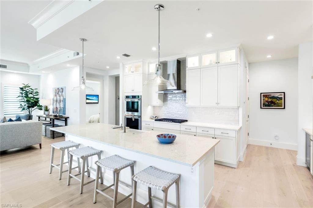 Kitchen featuring open floor plan, a breakfast bar, glass insert cabinets, light wood-style flooring, and light stone counters
