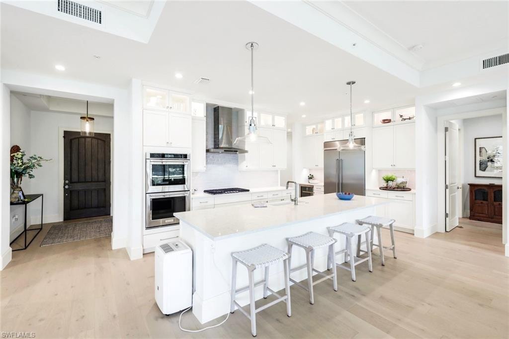 Kitchen with glass fronted cabinets, white cabinets, stainless steel appliances, and a kitchen breakfast bar