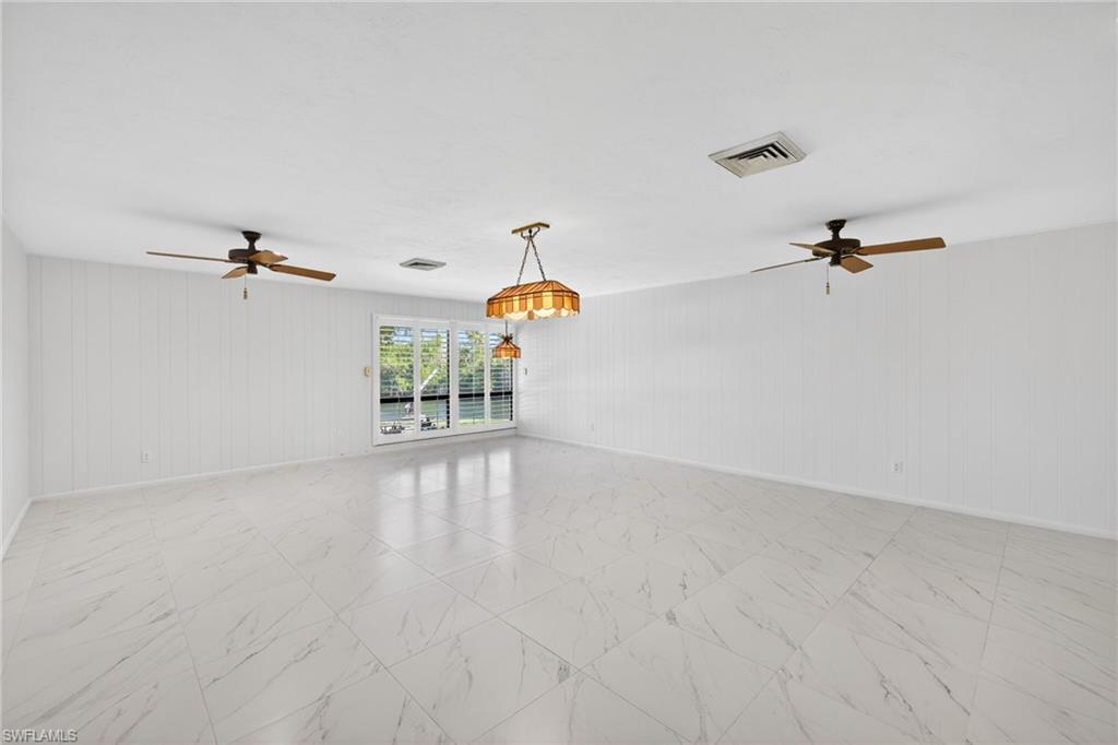 Spare room with a ceiling fan, wooden walls, and light marble finish floors