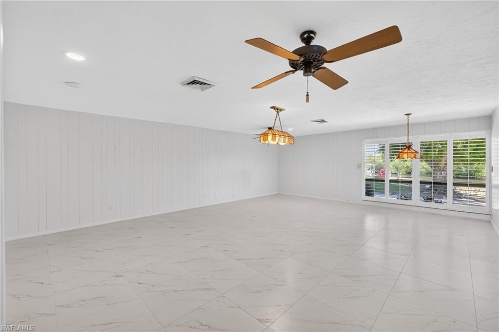 Unfurnished room with ceiling fan, wood walls, and light marble finish flooring