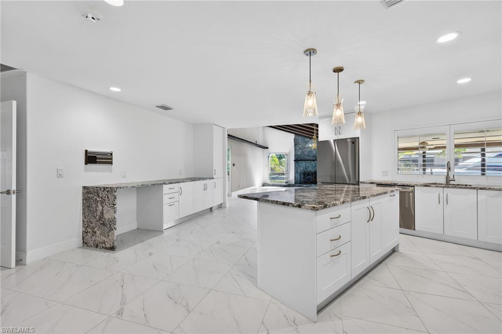 Kitchen with dark stone countertops, light marble finish floors, and a kitchen island