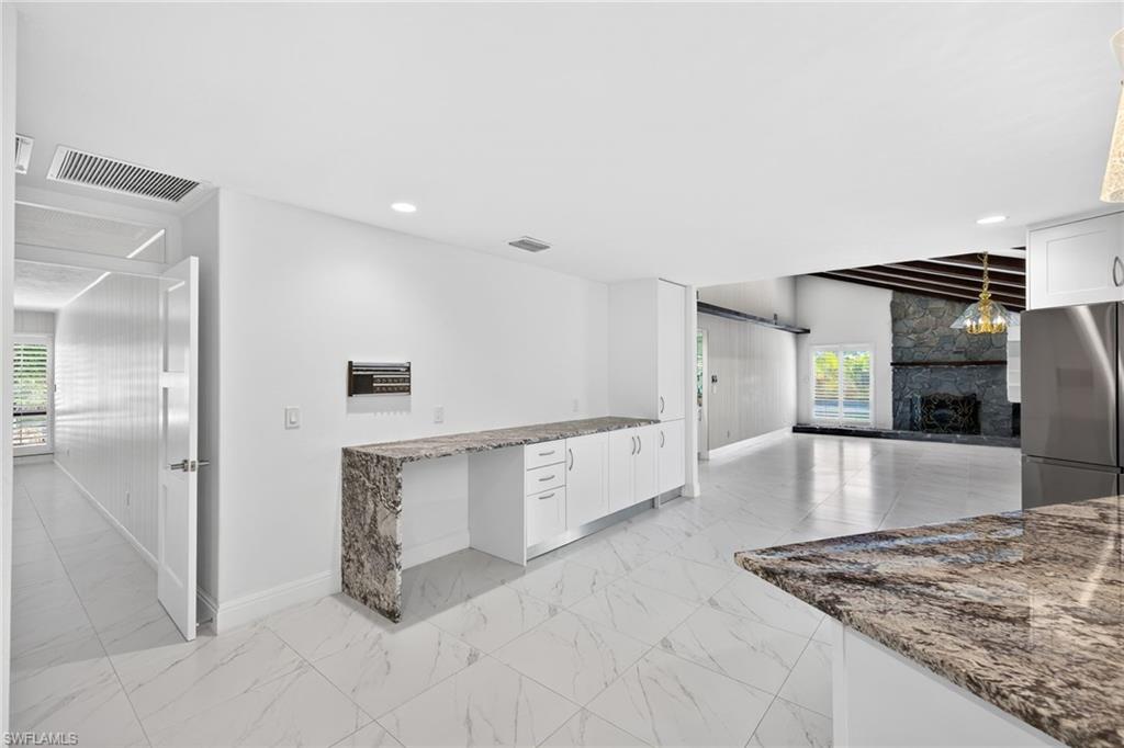 Kitchen with dark stone counters, white cabinets, a stone fireplace, freestanding refrigerator, and open floor plan
