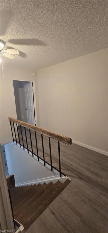 Stairway featuring wood finished floors, a textured ceiling, and ceiling fan