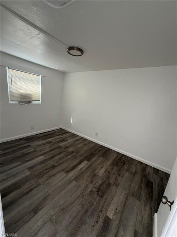 Spare room with dark wood-type flooring and baseboards
