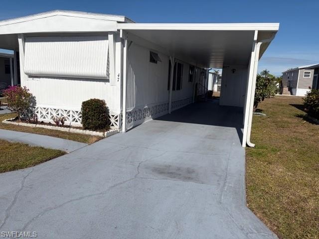 View of side of home with concrete driveway, an attached carport, a porch, and a yard