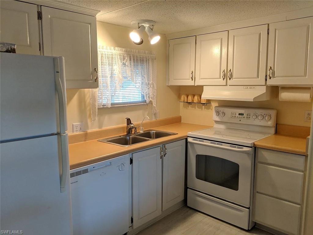 Kitchen with white appliances, light countertops, white cabinetry, and a textured ceiling