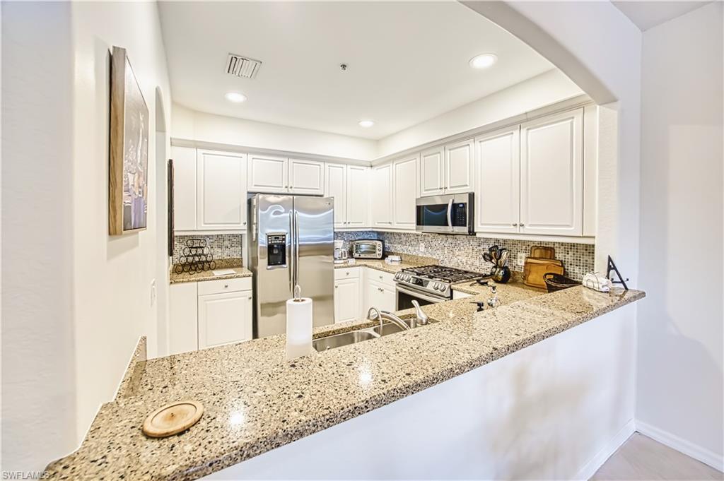 Kitchen featuring decorative backsplash, stainless steel appliances, light stone counters, white cabinetry, and recessed lighting