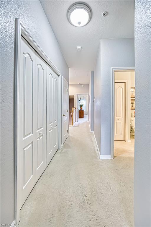 Hall featuring a textured wall, a textured ceiling, and light colored carpet