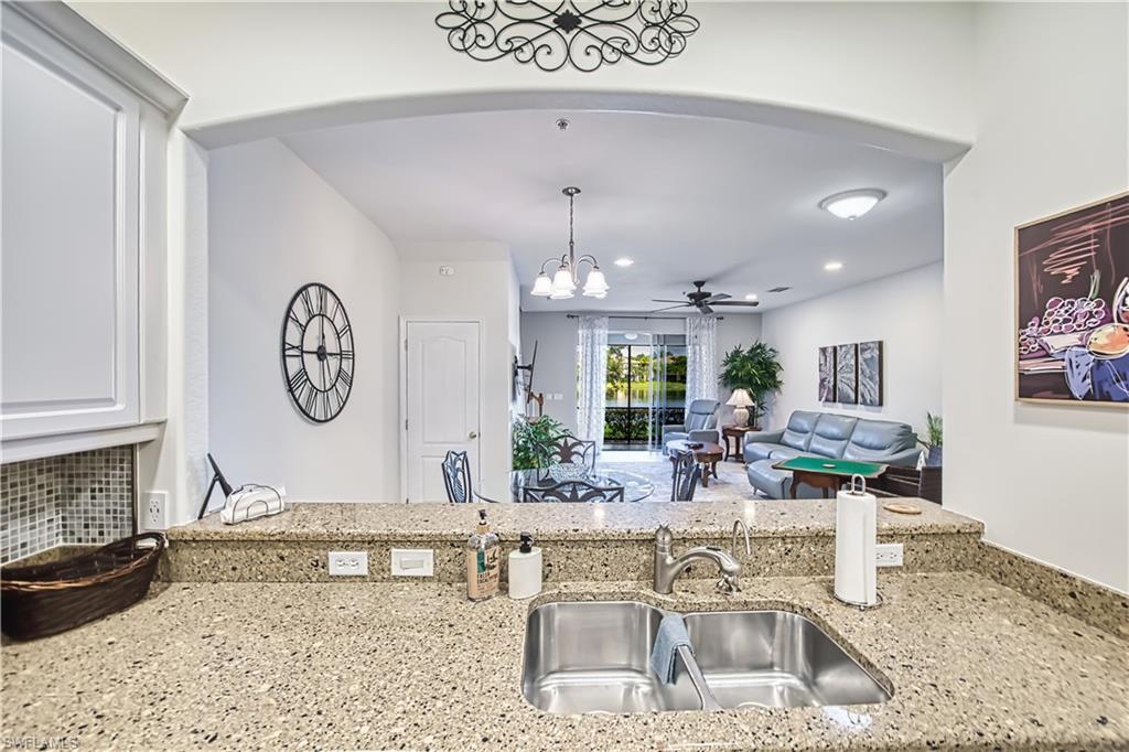 Kitchen featuring a ceiling fan, light stone counters, suspended lighting, arched walkways, and tasteful backsplash