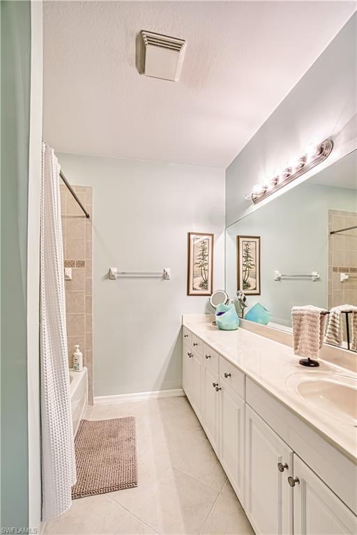 Bathroom featuring shower / bath combo, double vanity, light tile patterned floors, and a textured ceiling