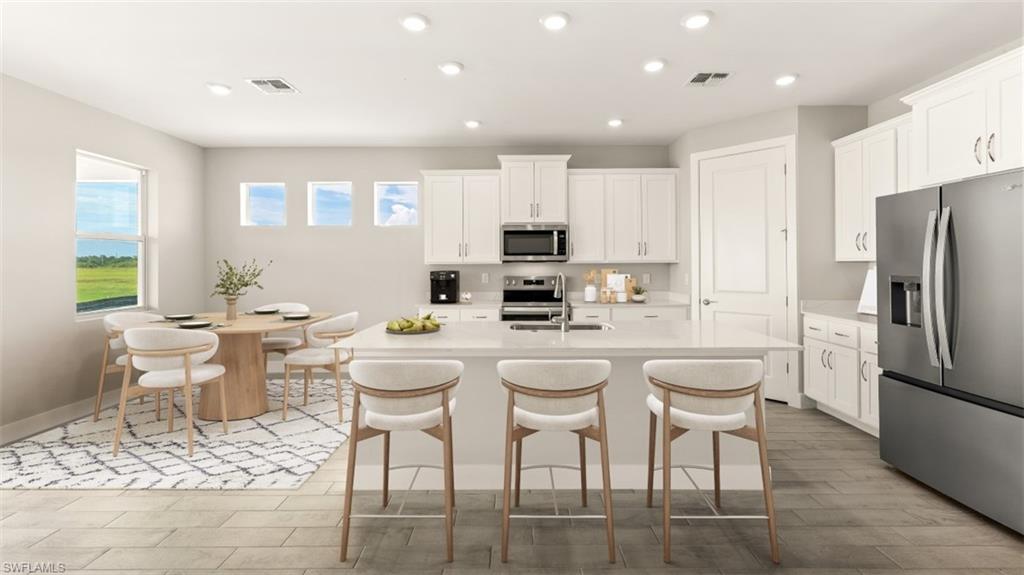 Kitchen featuring white cabinetry, stainless steel appliances, a center island with seating, recessed lighting, and wood-finish flooring