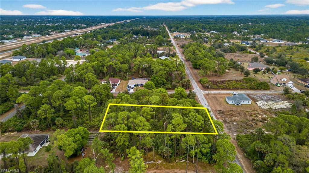 Aerial view of property and surrounding area featuring property parcel outlined and a forest