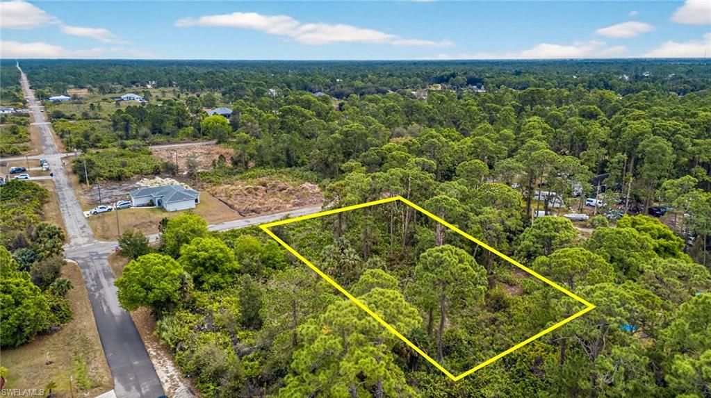 Aerial view of property and surrounding area featuring property parcel outlined and a heavily wooded area