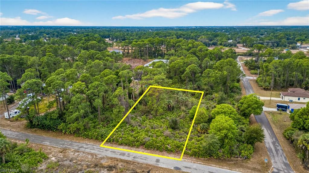 Aerial view of property and surrounding area featuring property parcel outlined and a heavily wooded area
