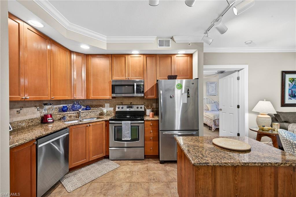 Kitchen with ornamental molding, dark stone countertops, stainless steel appliances, wood finish cabinetry, and tasteful backsplash