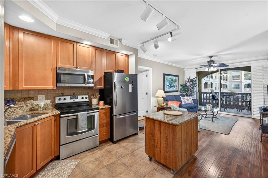 Kitchen featuring crown molding, wood finish cabinets, stainless steel appliances, light stone counters, and track lighting