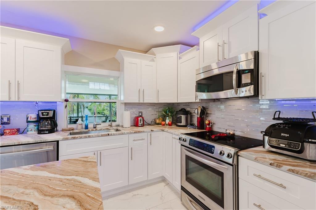 Kitchen with stainless steel appliances, white cabinets, light stone counters, recessed lighting, and light marble finish flooring