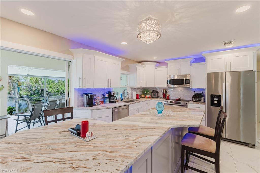 Kitchen featuring stainless steel appliances, a breakfast bar area, light stone countertops, white cabinets, and hanging lights