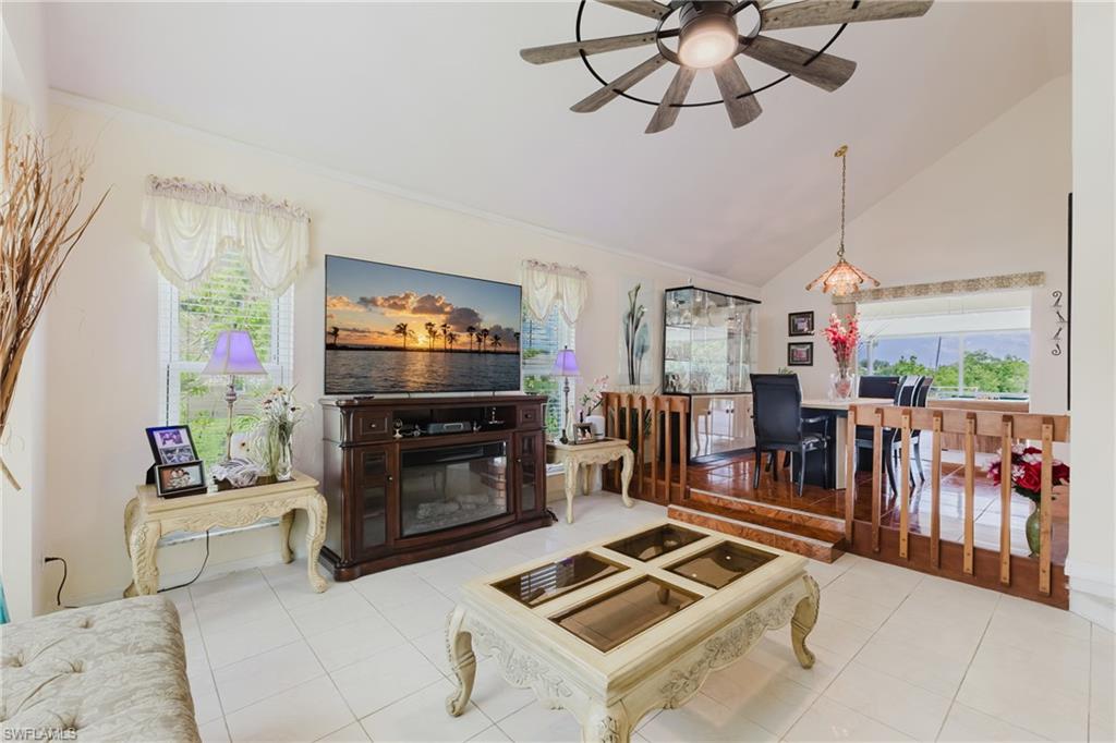 Living area with a glass covered fireplace, vaulted ceiling, a ceiling fan, and tile patterned flooring
