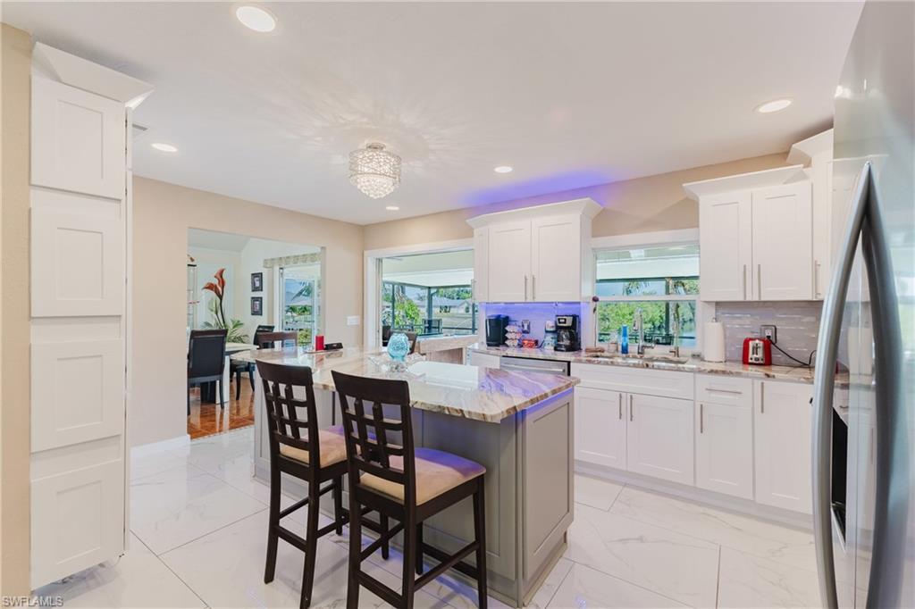 Two tone kitchen featuring a center island, stainless steel fridge, a kitchen breakfast bar, light stone counters, and light marble finish flooring