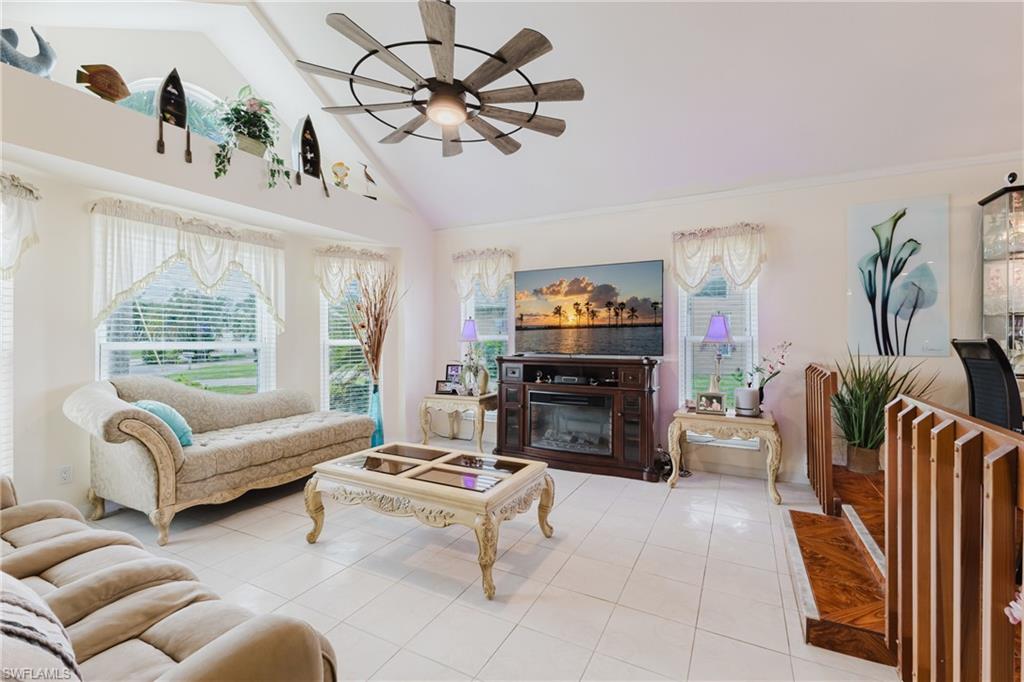 Living area with ceiling fan, tile patterned floors, vaulted ceiling, and a glass covered fireplace
