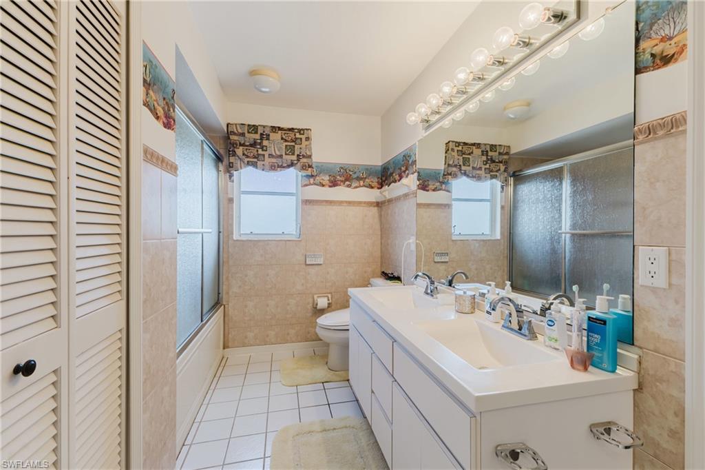 Full bathroom featuring double vanity, a closet, tile walls, light tile patterned floors, and bath / shower combo with glass door