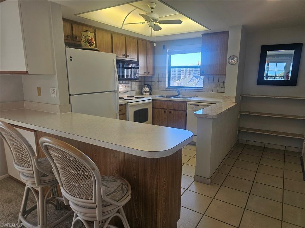 Kitchen featuring a peninsula, a kitchen bar, white appliances, wood finish cabinets, and tasteful backsplash