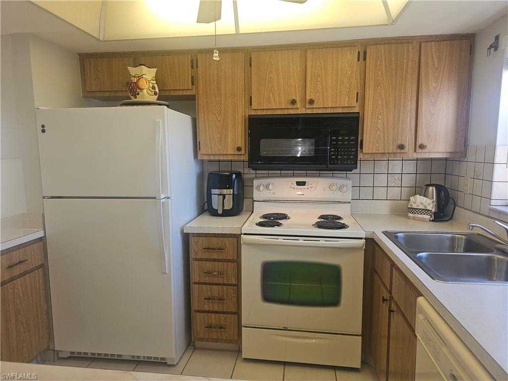 Kitchen featuring white appliances, light countertops, wood finish cabinetry, tasteful backsplash, and light tile patterned floors