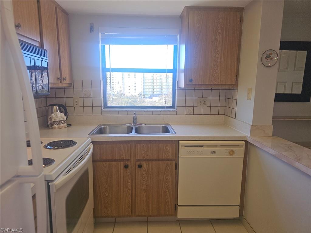 Kitchen featuring light countertops, white appliances, light tile patterned floors, and plenty of natural light