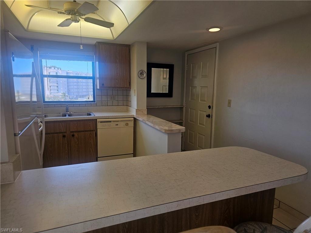 Kitchen featuring light countertops, freestanding refrigerator, white dishwasher, ceiling fan, and decorative backsplash