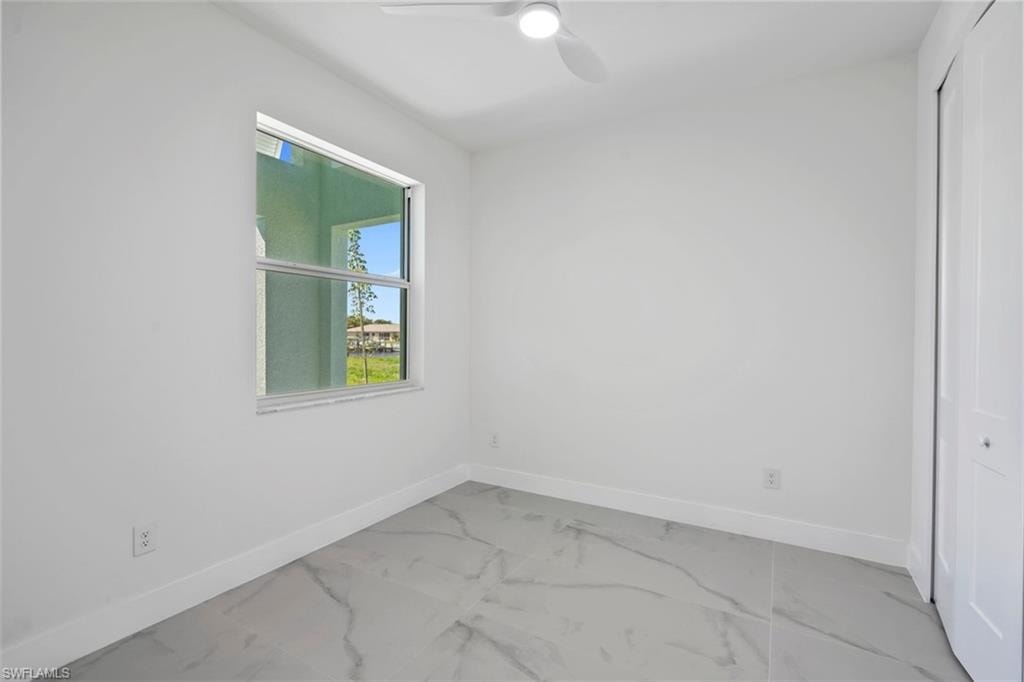 Spare room with marble finish floor, baseboards, and ceiling fan