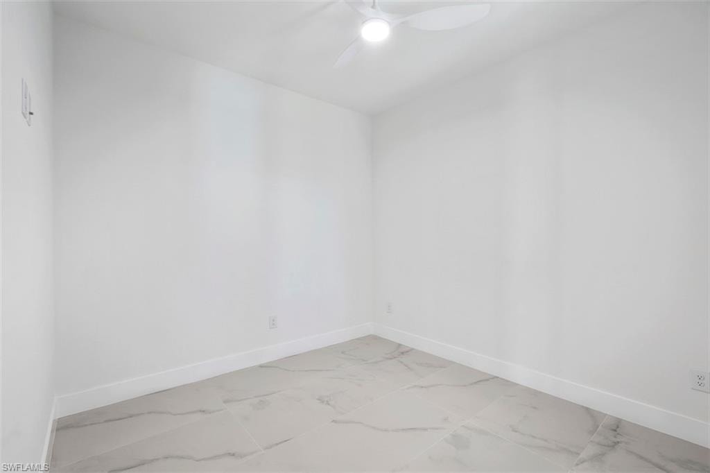 Unfurnished room featuring marble finish floor, baseboards, and ceiling fan