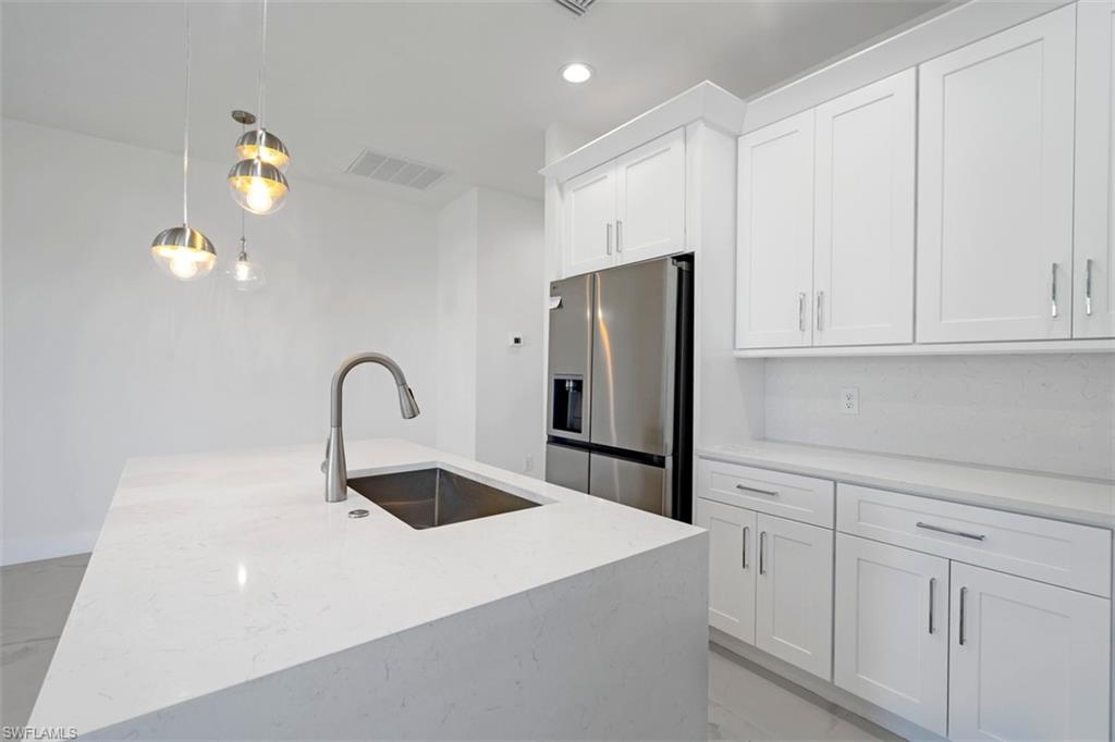 Kitchen featuring white cabinets, visible vents, a sink, stainless steel fridge with ice dispenser, and pendant lighting