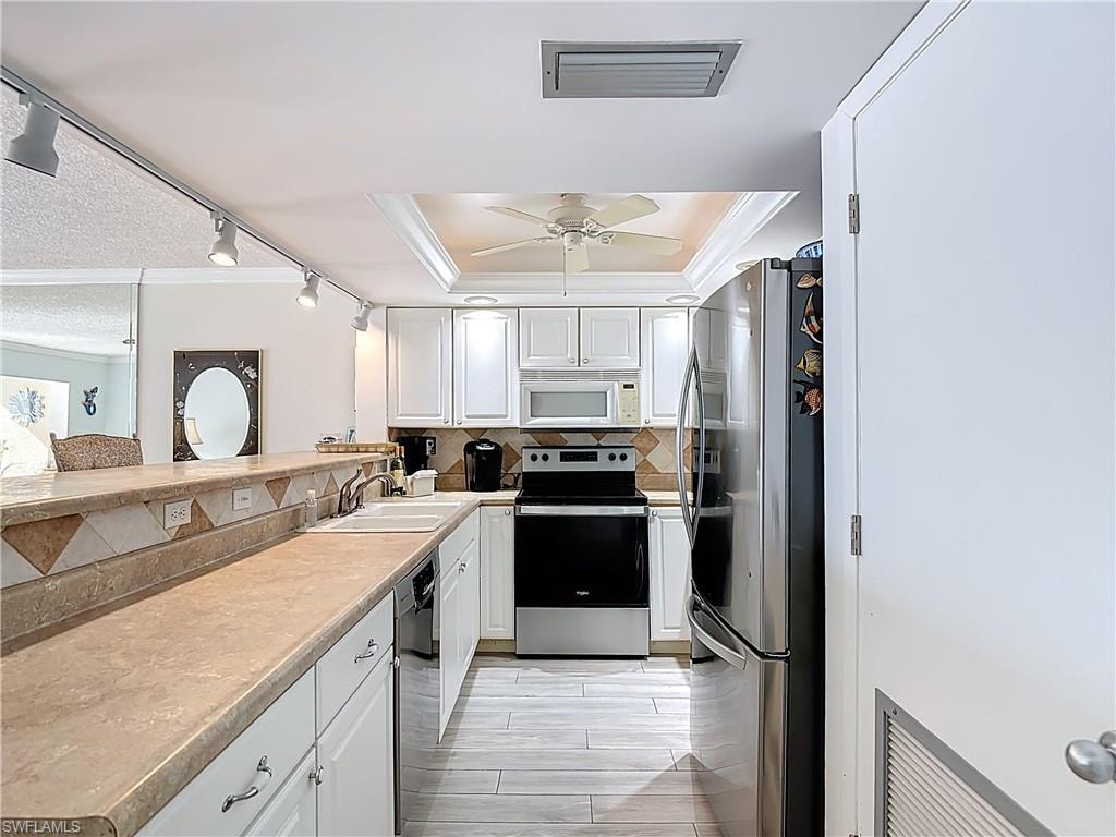 Kitchen with crown molding, white cabinets, stainless steel appliances, light countertops, and decorative backsplash