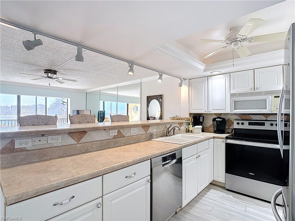 Kitchen with ceiling fan, crown molding, stainless steel appliances, white cabinets, and rail lighting
