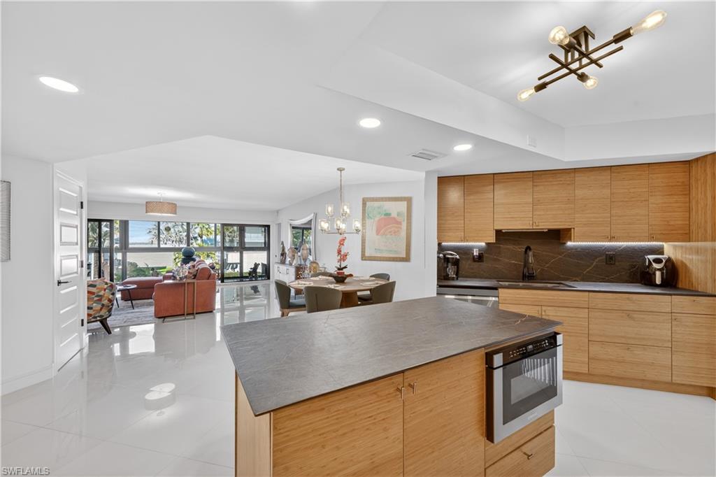 Kitchen with modern cabinets, open floor plan, hanging lights, backsplash, and stainless steel appliances