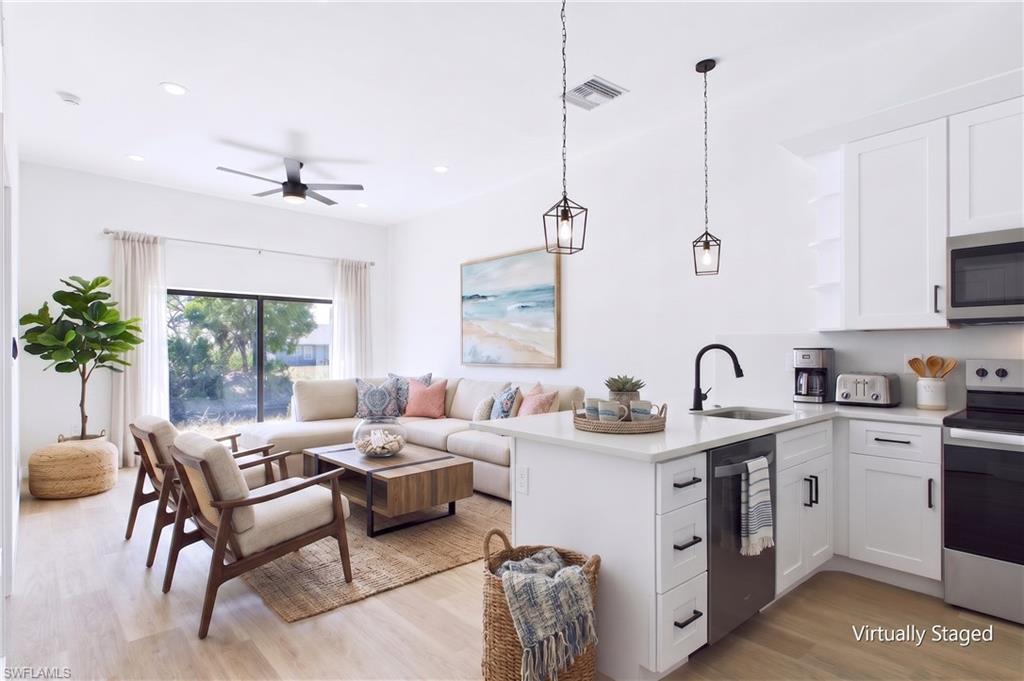 Open-concept living area featuring a kitchen island with sink, white shaker cabinetry, stainless steel appliances, and light wood-finish flooring
