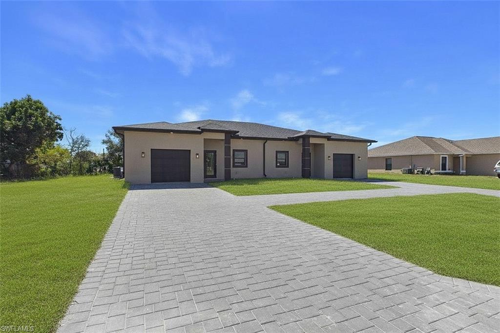 Prairie-style home featuring a front lawn, a garage, decorative driveway, and stucco siding