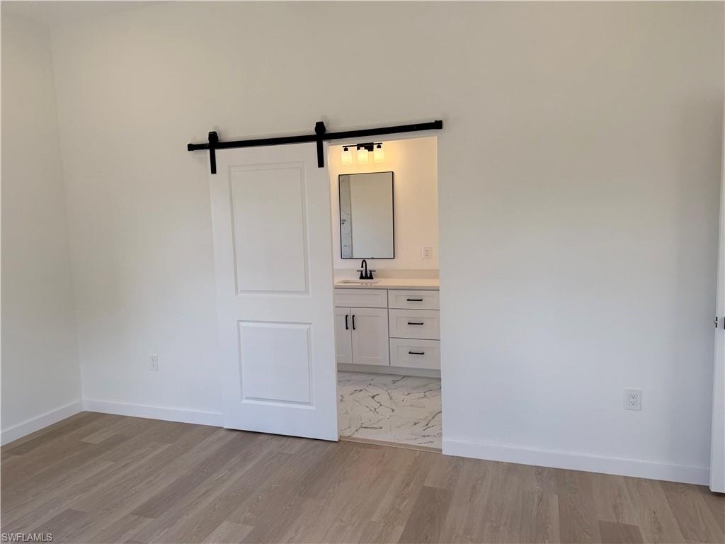 Unfurnished bedroom with a barn door, light wood-style flooring, and connected bathroom