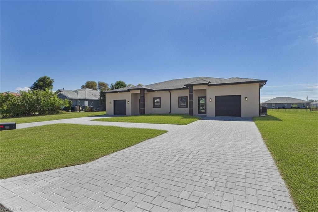 View of front of property with a front yard, decorative driveway, a garage, and stucco siding