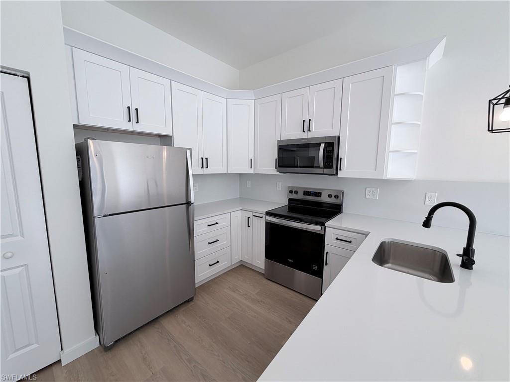 Kitchen with stainless steel appliances, open shelves, white cabinets, and light wood-style floors