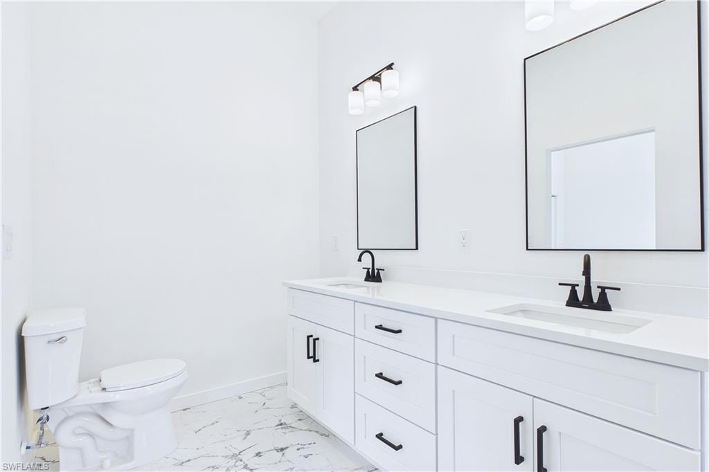 Full bath featuring double vanity and light marble finish floors