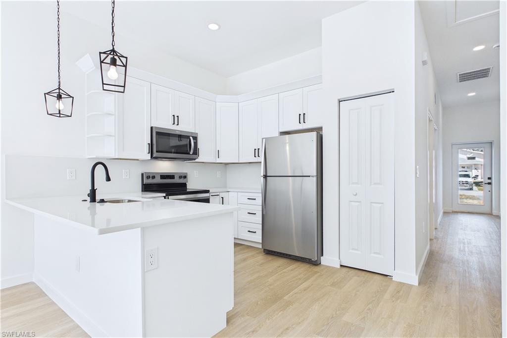 Kitchen with stainless steel appliances, open shelves, white cabinets, decorative light fixtures, and light wood finished floors