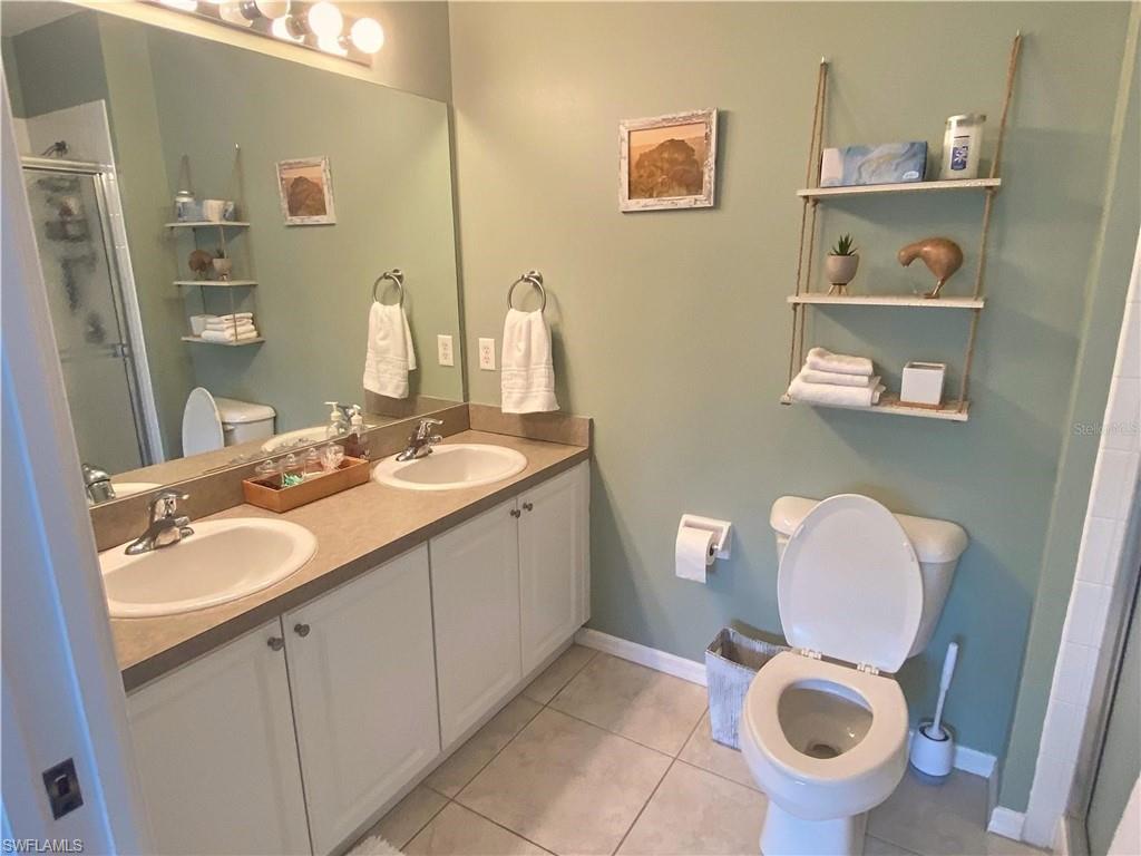 Full bathroom featuring a shower stall, double vanity, and light tile patterned floors