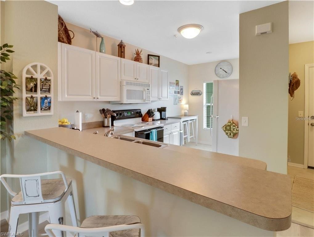 Kitchen with a peninsula, a kitchen bar, white appliances, and white cabinetry
