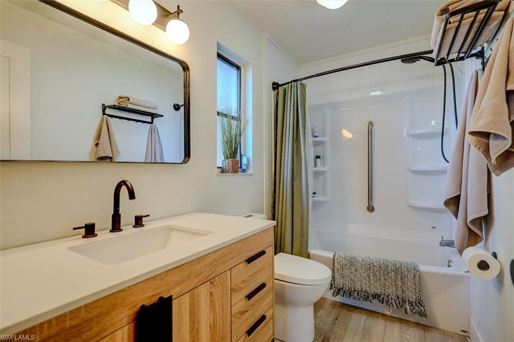 Full bathroom featuring hardwood / wood-style floors, vanity, shower / bath combination with curtain, and toilet