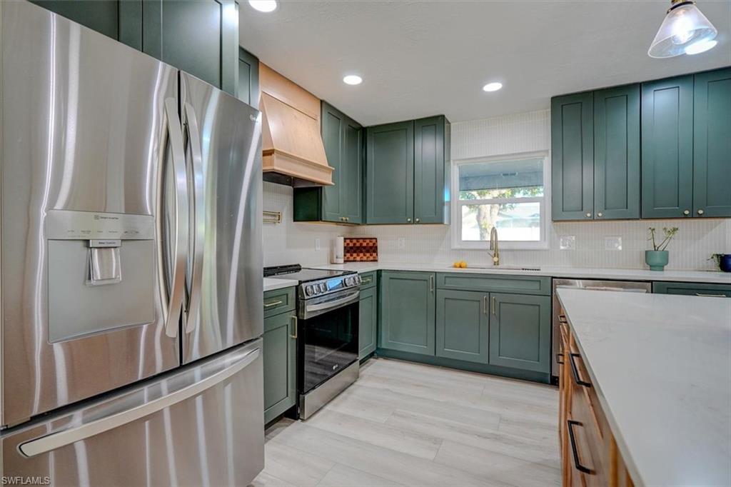 Kitchen with custom range hood, stainless steel appliances, green cabinetry, and sink