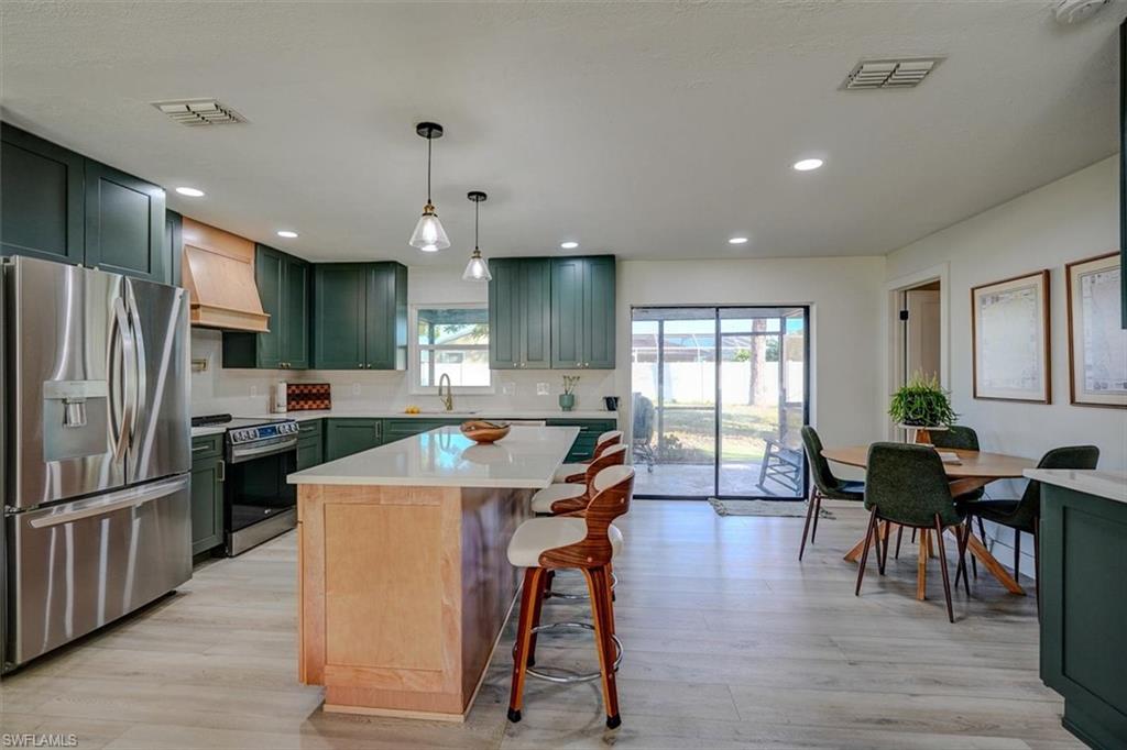 Kitchen with a breakfast bar, hanging light fixtures, light hardwood / wood-style floors, custom range hood, and stainless steel appliances